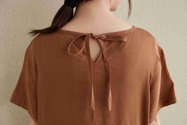 Puede incluir: Un vestido de lino marr&oacute;n con un escote de llave y un lazo en la espalda.