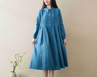 May include: A long-sleeved, blue linen dress with a collared neckline and button closure. The dress has a slightly flared skirt and a relaxed fit.