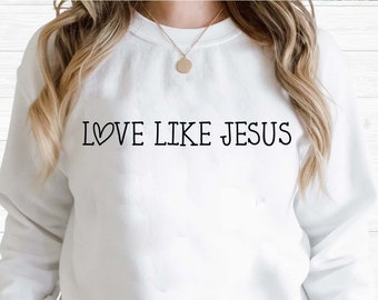 Può includere: Felpa bianca con il testo "LOVE LIKE JESUS" in lettere nere con un simbolo di cuore.