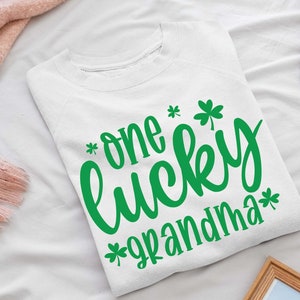 K&ouml;nnte beinhalten: Wei&szlig;er Pullover mit gr&uuml;nen Kleeblatt-Designs und dem Text "*one lucky grandma*"