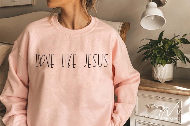May include: A pink sweatshirt with the text "LOVE LIKE JESUS" in black lettering. The text includes a small heart symbol.