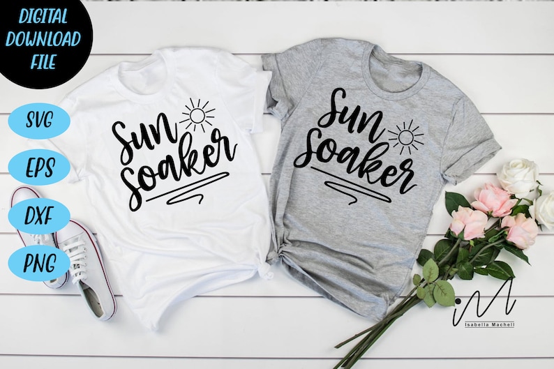 Peut inclure: Deux t-shirts blancs avec le texte "Sun Soaker" en &eacute;criture noire avec un petit graphique de soleil. Les chemises sont dispos&eacute;es sur une surface en bois blanc avec un bouquet de fleurs roses et blanches.