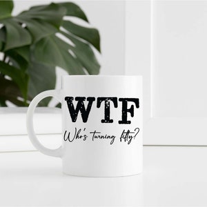 May include: White ceramic coffee mug with black text that reads "WTF Who's turning fifty?"