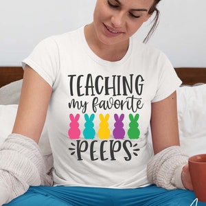 May include: A white t-shirt with the text "TEACHING my favorite PEEPS" in black. The text is surrounded by five colorful marshmallow bunny images.