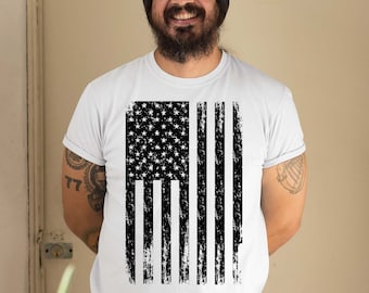 May include: A white t-shirt with a black and white distressed American flag design. The flag is centered on the shirt and has a vintage look.