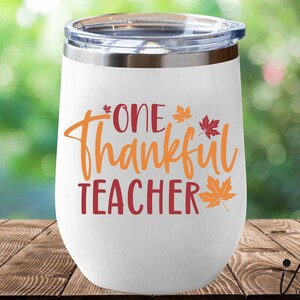 May include: White stainless steel wine tumbler with a red and orange design that says "One Thankful Teacher" with fall leaves.