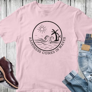 Peut inclure: Un t-shirt rose avec un motif circulaire noir repr&eacute;sentant un soleil, des palmiers, des vagues et le texte "Happiness comes in waves".