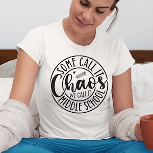 Puede incluir: Camiseta blanca con un gr&aacute;fico circular negro que dice "Some call it chaos we call it middle school" con un l&aacute;piz y un coraz&oacute;n dentro del c&iacute;rculo.