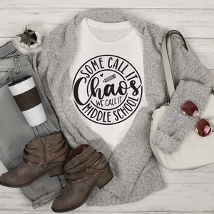 Puede incluir: Camiseta blanca con un dise&ntilde;o circular negro que dice "Some call it Chaos We call it Middle School" con un l&aacute;piz y un coraz&oacute;n gr&aacute;fico.