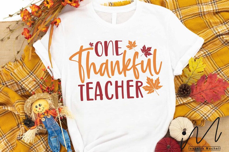 May include: White t-shirt with the text "One Thankful Teacher" in orange and red lettering. The text is surrounded by small red and orange maple leaves.