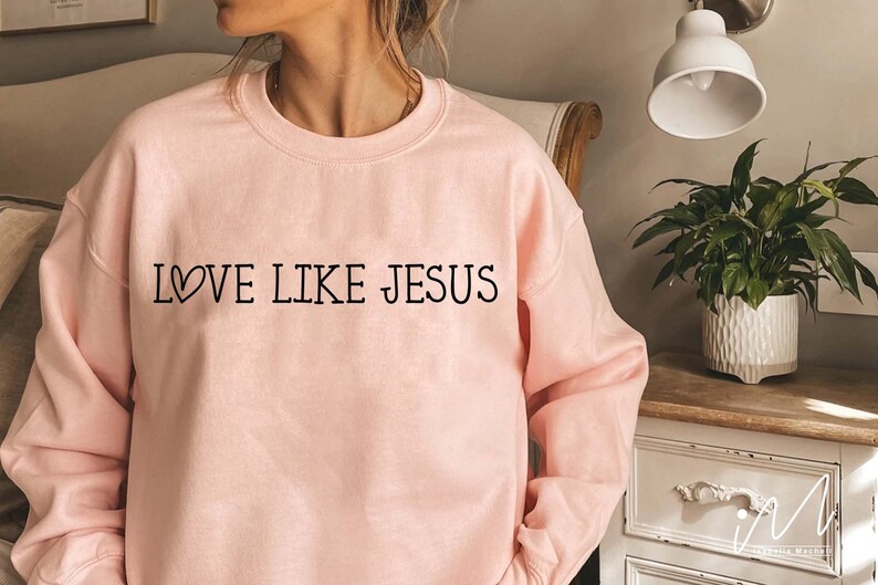 May include: A pink sweatshirt with the text "LOVE LIKE JESUS" in black lettering with a small heart symbol before the word "LOVE".