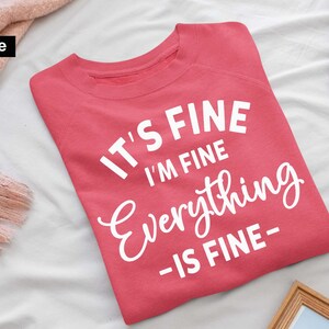 May include: A coral-colored crewneck sweatshirt featuring the white printed text IT'S FINE I'M FINE Everything -IS FINE- centered on the front. The garment has long sleeves and a ribbed neckline, presented as a digital file for design purposes.