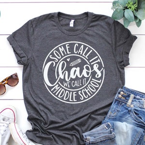 Puede incluir: Una camiseta gris con un dise&ntilde;o circular blanco que dice "Some call it chaos we call it middle school".