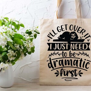 May include: A beige tote bag with a black graphic of a sloth and the text "I'll get over it I just need to be dramatic first".