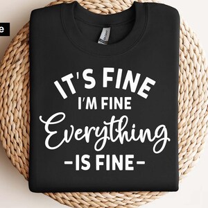 May include: A black crew neck t-shirt featuring white text that reads IT'S FINE I'M FINE Everything IS FINE. The shirt has a standard collar with a visible brand tag inside the neckline and is presented as a digital file for printing purposes.