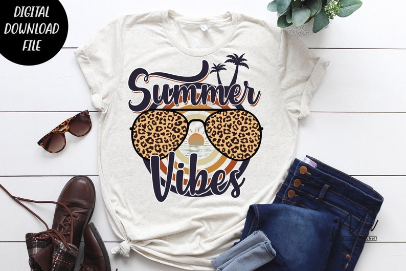 May include: A white t-shirt with the text "Summer Vibes" in blue and black lettering. The text is surrounded by a circle with a sunset and palm trees. The circle is decorated with a leopard print pattern.