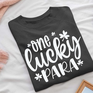 May include: A dark gray sweatshirt with the text "one lucky PARA*" in white lettering. The text is in a cursive font and includes a shamrock graphic.