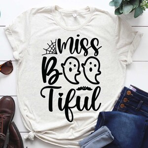 May include: A light-colored t-shirt with the words "miss Boo-tiful" in black script, featuring two ghost illustrations and a spiderweb. The shirt is part of a digital download file, with SVG, EPS, DXF, and PNG file formats.
