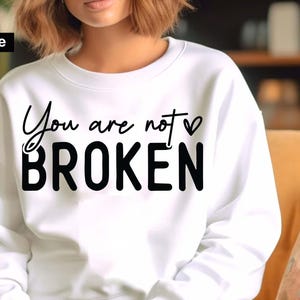 May include: White sweatshirt with the text "You are not BROKEN" in black script. The word "not" has a small heart symbol above it. The words are centered on the front of the sweatshirt.