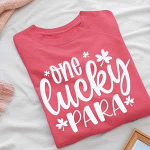 May include: A pink sweatshirt with the text "one lucky para" in white lettering with shamrock designs.