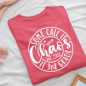 May include: A pink sweatshirt with a white circle design that says "Some call it chaos we call it 3rd grade" with a pencil and heart inside the circle.
