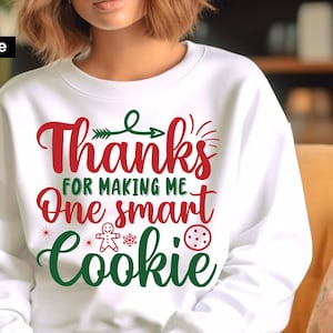 May include: White sweatshirt with red and green text that reads "Thanks for making me one smart cookie". The text is surrounded by a gingerbread man, snowflakes, and a cookie.