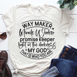 May include: A beige t-shirt with a black circle graphic that says "Way Maker Miracle Worker Promise Keeper Light in the Darkness My God That is Who You Are".