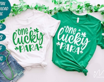 May include: Two white t-shirts with green shamrock designs. The text on the shirts reads "one lucky *PARA*" in green lettering. The shirts are laid out on a white surface with green garland.