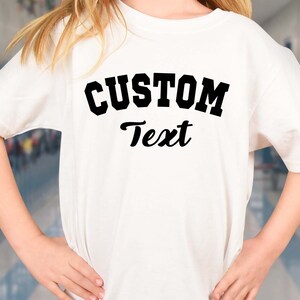 May include: White t-shirt with black text that says "CUSTOM Text" in a collegiate font.