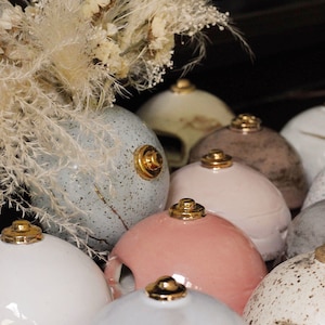 Könnte beinhalten: Eine Sammlung von Keramikkernhaltern mit goldenen Akzenten. Die Halter sind in verschiedenen Farben, darunter Weiß, Grau, Rosa und Braun. Jeder Halter hat ein kleines Loch oben zum Verbrennen von Räucherstäbchen.