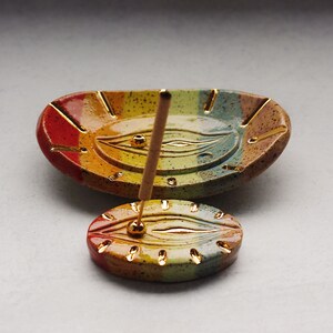 May include: A rainbow colored ceramic incense holder with a gold trim and a small round incense holder with a gold trim. The incense holder is shaped like an eye with a gold dot in the center.