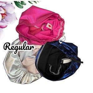 May include: Three satin bonnets in vibrant colors: hot pink, silver, and navy blue. Each bonnet has a drawstring closure. The word "Regular" is written in a cursive font.