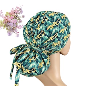 May include: A green and yellow patterned scrub cap featuring a repeating design of lizards and leaves. The cap is tied at the back with long ties. A bouquet of pink and purple flowers is in the background.