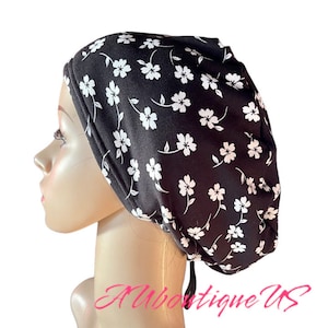 May include: A black scrub hat with a white floral pattern. The hat has a tie at the back.