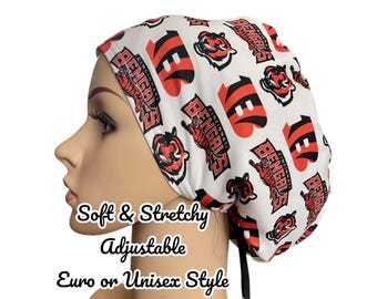 May include: A white and red Cincinnati Bengals print scrub cap. The cap features the team's logo and name. The cap is soft, stretchy, and adjustable. The text on the cap says "Soft & Stretchy, Adjustable, Euro or Unisex Style."