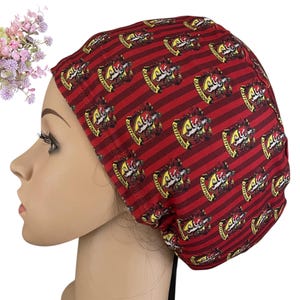 May include: Red and maroon striped scrub cap with a repeating crest pattern. The crest features a lion and the text "Gryffindor". The cap is made of a soft fabric and is designed to fit comfortably.