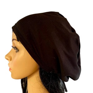 May include: A black cotton beanie with a gathered top and a drawstring tie. The beanie is worn on a mannequin with long black hair.