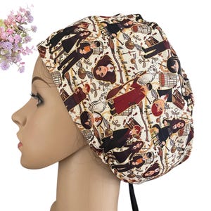 May include: A beige scrub cap featuring a repeating pattern of characters, owls, and other imagery. The cap is tied in the back with a black drawstring. A small bouquet of pink and purple flowers is in the upper left corner.