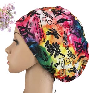 May include: A colorful scrub cap with a vibrant watercolor design. The cap features various symbols and text, including "Platform 9 3/4" and the letters "HP". The design includes images of glasses, feathers, and other magical elements.