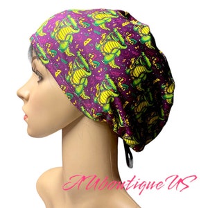 May include: Purple surgical scrub hat with a green and yellow alligator print. The hat has a tie at the back.