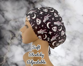 May include: Black adjustable scrub cap featuring a pattern of white skeleton hands, planchette, crescent moons, and stars. The cap is soft and stretchy. Text on the image reads "Soft, Stretchy, Adjustable."