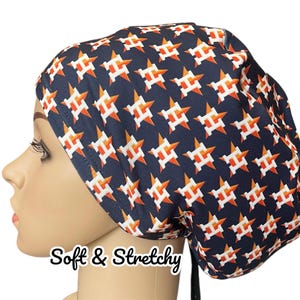 May include: A blue and orange patterned scrub hat with a white star and letter H design. The hat has a tie at the back. "Soft & Stretchy" is written in white text at the bottom of the image.