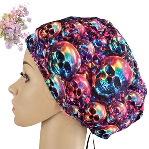 May include: A colorful skull print bouffant scrub cap. The cap features a repeating pattern of skulls in shades of blue, purple, orange, and yellow. The cap is tied at the back with black ties. A small bouquet of pink and purple flowers is in the upper left corner.