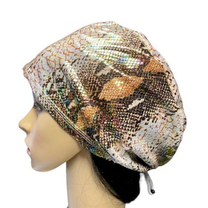 May include: A white, brown, and iridescent surgical scrub hat with a snake skin pattern. The hat has a drawstring tie at the back.