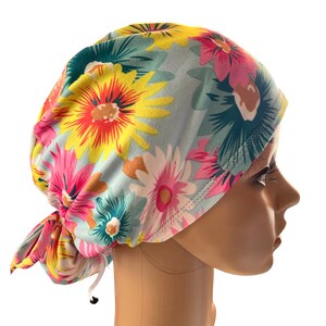May include: A floral patterned scrub cap featuring a light blue background with large, colorful flowers in shades of pink, yellow, and white. The cap is tied at the back with a drawstring for an adjustable fit. The cap is designed to be worn in a medical setting.