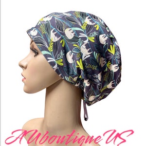 May include: A dark gray scrub cap featuring a pattern of white sloths, green and yellow leaves, and white floral elements. The cap has a drawstring for adjustment and is shown on a mannequin head. The text "Aboutique US" is at the bottom.