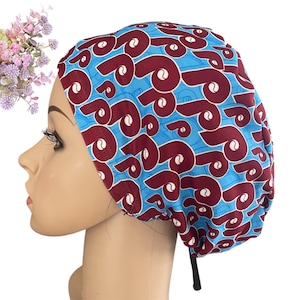 May include: A blue and maroon patterned bouffant scrub cap. The cap features a repeating design of maroon swirls on a light blue background. The cap is designed to be worn in a medical or professional setting.