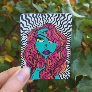 May include: A sticker featuring a psychedelic illustration of a woman with pink hair and a third eye. The background is a black and white wavy pattern.