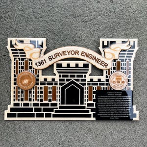 May include: Wooden plaque with a black and brown castle design, featuring the text "1361 SURVEYOR ENGINEER." Includes two circular emblems and a black rectangular plaque with text. The plaque is likely a military or service recognition item.