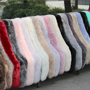 May include: A collection of faux fur scarves in various colours, including red, pink, white, grey, and blue. The scarves are arranged in a row on a wooden bench.